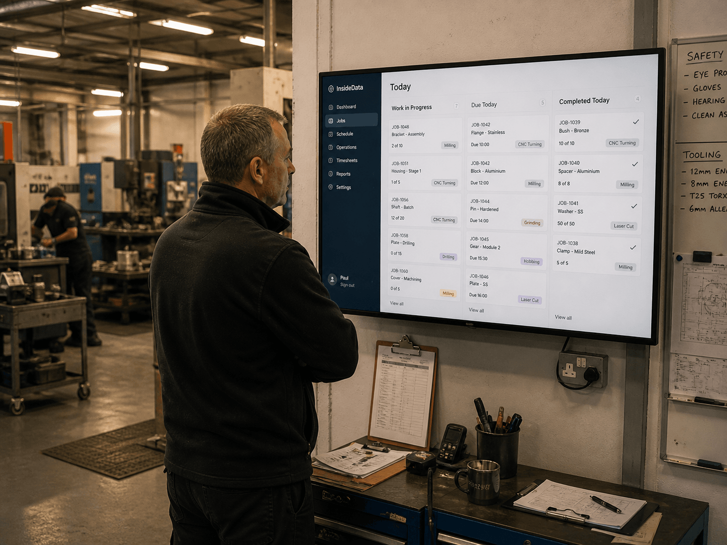 An operations manager reviewing today’s job board on a wall-mounted screen in a workshop.